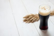 glass of dark beer with wheat on a white wooden table background with copy space for text