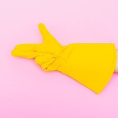 Poster - the hand in the yellow glove depicts the gesture of a gun on pink background. minimalism and surrealism