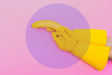 Wall Mural - hand in yellow glove is holding a banana like a gun on a pink background. violet or purple circle in the middle for text. minimalism and surrealism. crerative conceptual