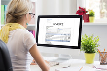 Woman In Office With Sample Invoice Document On Computer