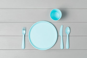 Poster - Set of empty, pastel plastic tableware bowls, spoons, knifes and forks isolated on gray wooden background. Flat lay, top view with minimal style.