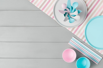 Poster - Set of empty, pastel plastic tableware bowls, spoons, knifes and forks isolated on gray wooden background. Flat lay, top view with minimal style.