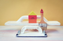 The Concept Of Renovation In The Apartment. A Spatula, A Paintbrush And A Toy House.