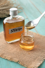 Wall Mural - glass bottle of syrup with spoon on blue wooden background