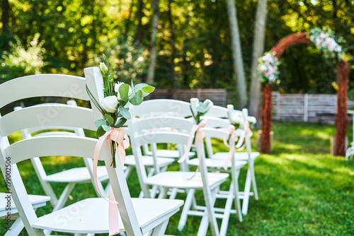Fotografía White fresh flowers with pink ribbon on wedding chair on each side of archway outroods; copy space