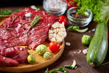 Wall Mural - Still life of raw beef meat with vegetables on wooden plate over vintage background, top view, selective focus