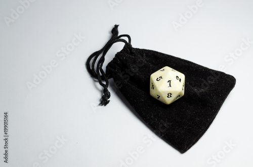 white twenty-sided dice on a small black purse on a white background плакат