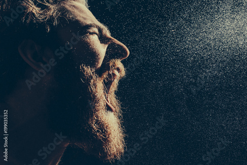 Fotografía A bearded man angrily screams into a spray of water against a black background