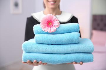 Wall Mural - Young maid holding stack of towels and flower in hotel room