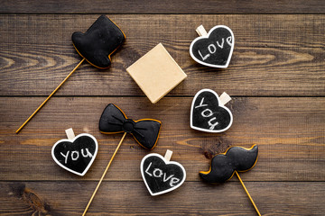 Gift for man on birthday. Gift box among cookies in shape of moustache, hat, bow tie and hearts with lettering love you on dark wooden background top view copy space