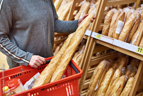 Plakat Buyer with baguettes in basket at store