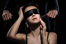 Man In Suit Ties A Woman's Eyes With A Silk Ribbon On Black Background