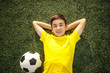 happy teenage boy with a soccer ball lying on the green lawn. Shot from top.