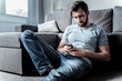 © Viacheslav Yakobchuk - Useless waiting. Sad cheerless handsome man sitting on the floor and looking at the smartphone screen while waiting for a message
