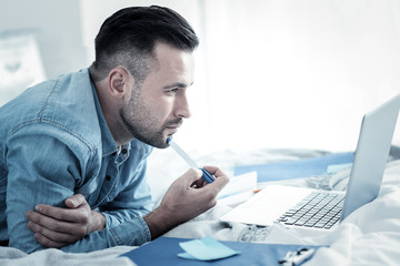 new ideas. serious handsome smart man holding a pen and looking at the laptop screen while thinking 