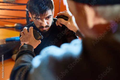 Photo  Portrait of bearded Middle-Eastern man boxing  with coach at practice in martial