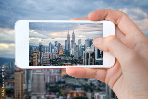 Obraz na plátne Closeup of a hand with smartphone taking a picture of Kuala Lumpur skyline, Mala