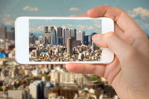 Fotografia, Obraz Closeup of a hand with smartphone taking a picture of Tokyo skyline, Shinjuku bu