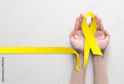 Fotomural Two hands holding yellow ribbon, symbol of cancer awareness, medical support and prevention with helping hand