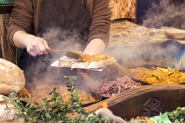 Man puts on a large piece of bread a lot of different food with seasonings and spices