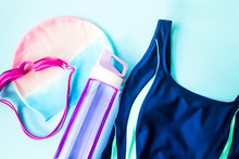Women's Accessories For Swimming In The Swimming Pool - Safety Glasses, A Hat, A Swimsuit And A Bottle Of Water On A Blue Background