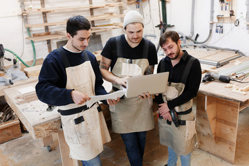 Master of small business with laptop and his team as sign of innovation in carpenter workshop. startup business, young specialist