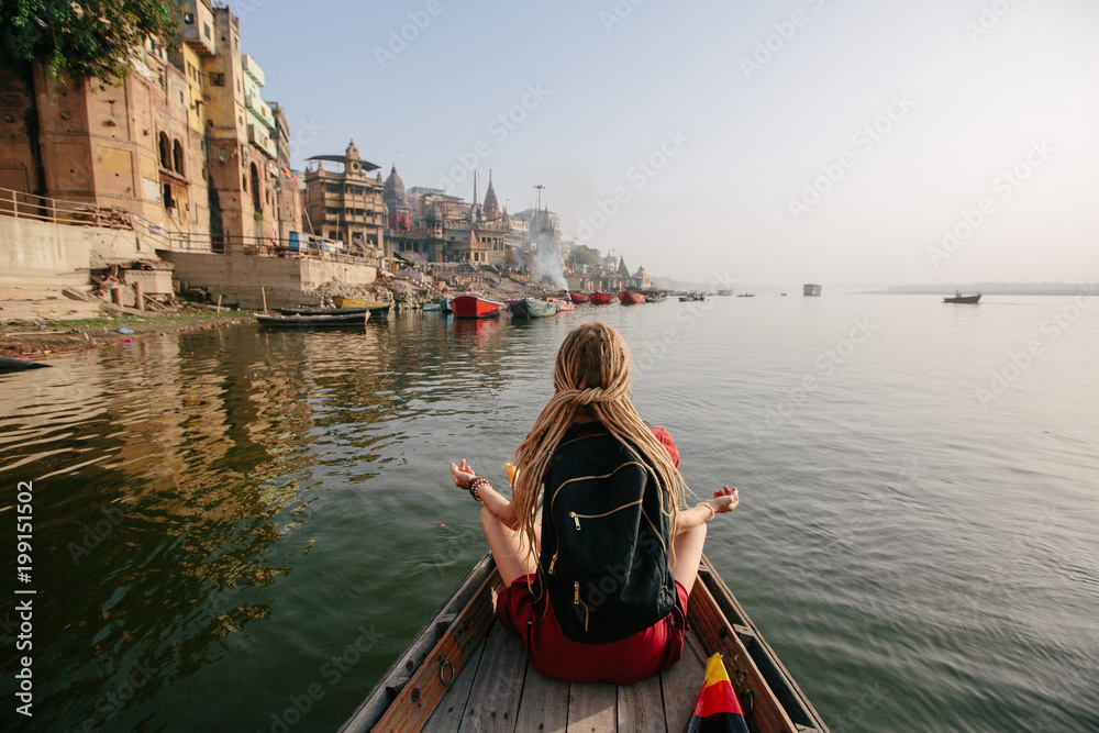 Traveler female wearing dreadlocks seating in wooden boat and enjoy Varanasi view - obrazy, fototapety, plakaty 