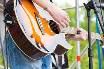 Musical band perfom on an open air festival. Guitarist man playing music by wooden acoustic guitar close-up