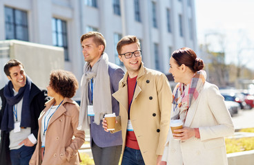 Canvas Print - business, education and corporate people concept - happy international group of office workers with conference badges drinking coffee and talking outdoors