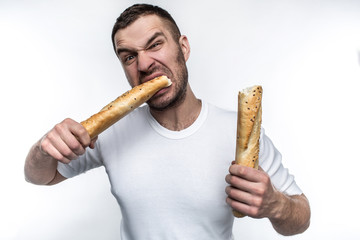 Very hungry man is starving. He broke a long piece of baguette into two pieces. He is eating one of this pieces. He looks brutal and weird. Isolated on white background.