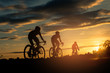 The men ride  bikes at sunset with orange-blue sky background. Abstract Silhouette background concept.
