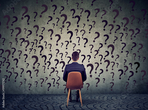 Fotomural business man sitting on a chair in front of a wall has many questions, wondering