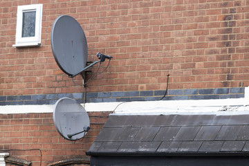 Two satelite dishes attached to a red brick wall