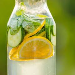 Wall Mural - healthy eating, drinks, diet. Detox drink from lemon and mint with cucumber on a background of green grass