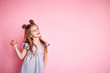 fashionable little girl with long brunette hair in pink dress holding a perfume, isolated on a pink background with copy space