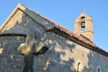 Stone cross of a grave with a belfry behind it