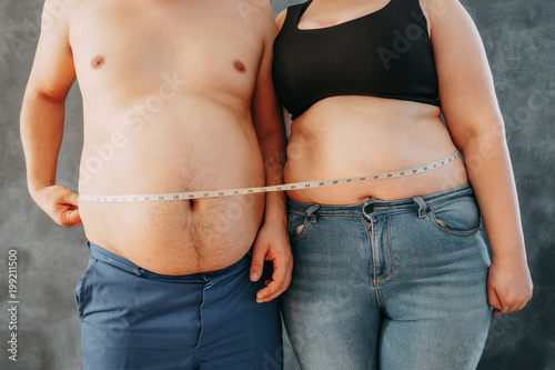 Cuadros en Lienzo Overweight couple standing together wrapped with measure tape
