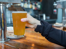 Woman Lifting Up Pint Glass Of IPA Beer In A Bar In A Brewery