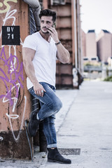 Wall Mural - Handsome young man standing outdoors in urban environment on metal stairs, talking on cell phone