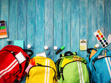 Colourful Children Schoolbags On Wooden Floor. Backpacks With School Accessories