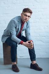 Fototapete - Stylish man in casual clothes sitting in front of brick wall
