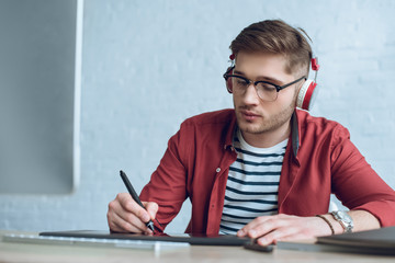 Fototapete - Freelancer man in headphones drawing with graphic tablet by table with computer