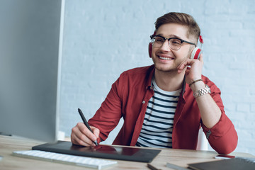 Fototapete - Smiling designer sitting by table with graphic tablet and computer