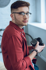 Fototapete - Bearded man holding digital camera by light window