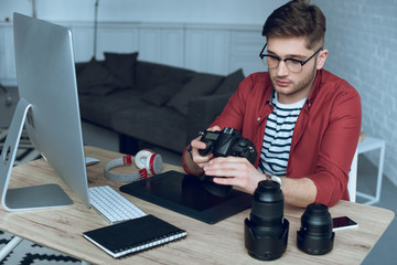 Fototapete - Man freelancer with camera in hands at work by table with computer and graphic tablet
