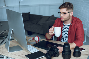 Fototapete - Young designer working by computer and drinking coffee