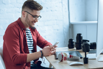 Fototapete - Happy freelancer man using smartphone sitting by working table