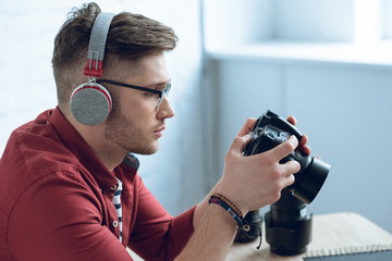 Fototapete - Young bearded man in headphones holding camera by table