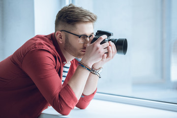Fototapete - Young photographer shooting with digital camera by light window