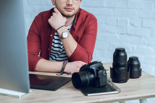 Bearded man sitting by table with camera and graphic tablet